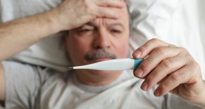 Older man sick in bed taking his temperature