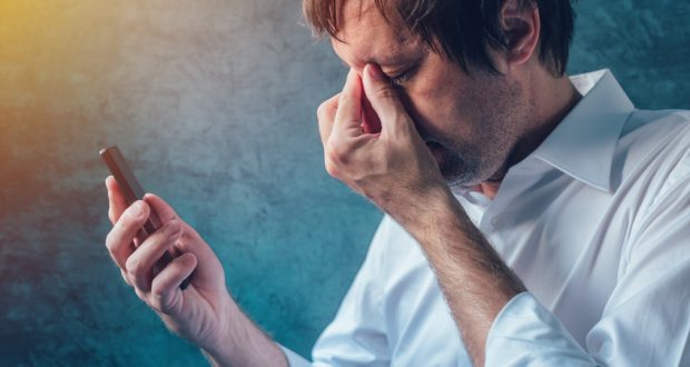 Tired man with headache staring at cell phone