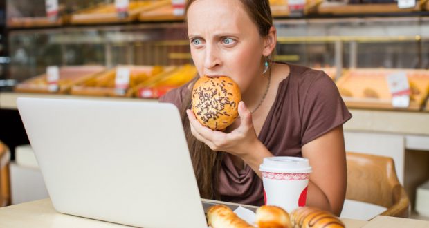 Young woman eating pastry stressed in front of computer