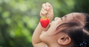 Happy young girl eating a strawberry