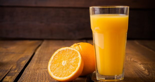 glass of orange juice and fresh orange on wooden table