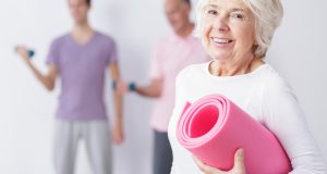 Older woman smiling with yoga mat