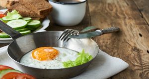 Fried egg in bowl with knife and fork on wooden table