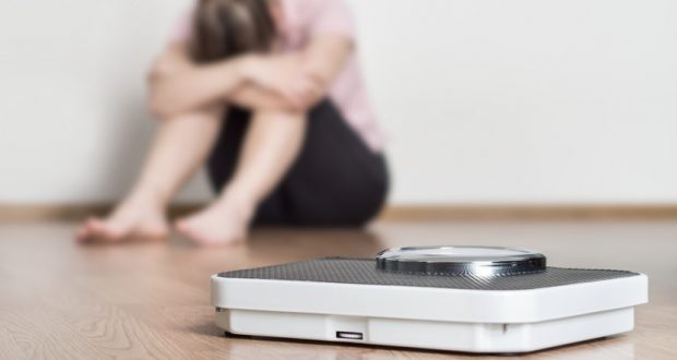 Disappointed woman sitting on floor next to scale