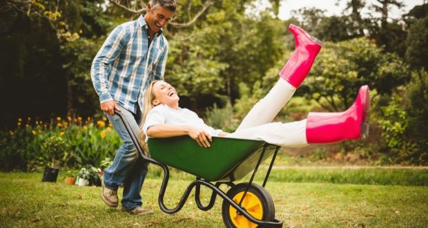 Smiling man pushing laughing woman in wheelbarrow