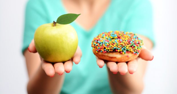 One hand holding an apple the other hand holding a sprinkle doughnut