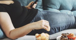 Woman lying on couch eating chips